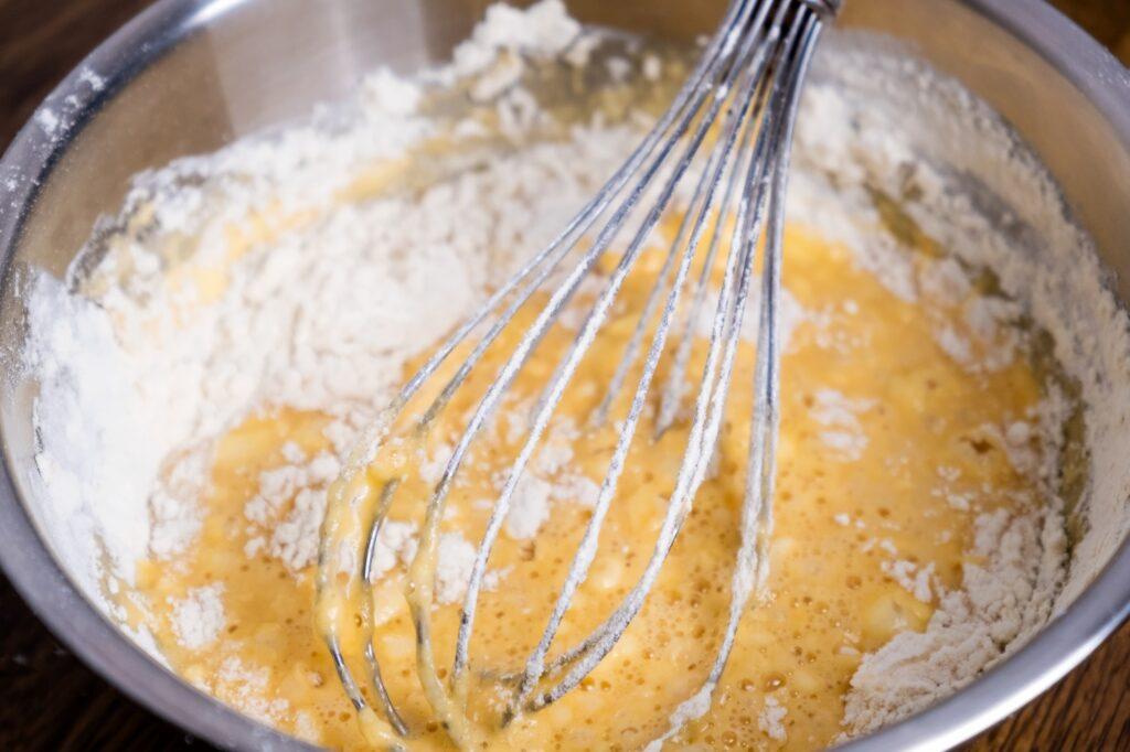 Bowl of batter and whisk on wooden table