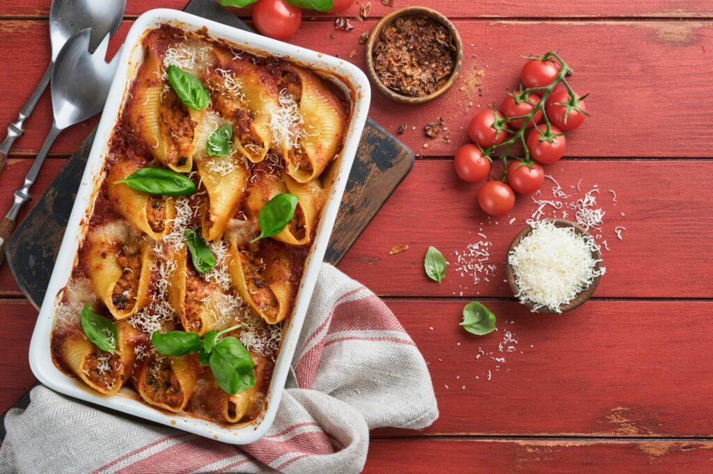 Cannelloni or conchiglioni. Baked stuffed pasta shells with bolognese meat sauce, tomatoes, basil on