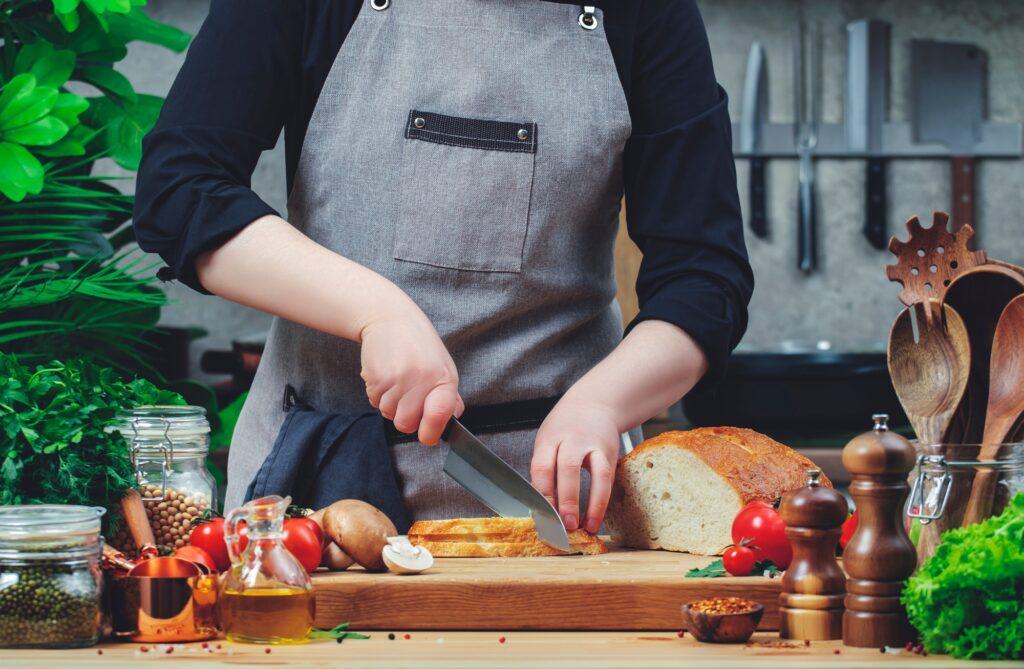 Blogger chef cutting white wheat bread on cozy kitchen with wooden table, kitchenware