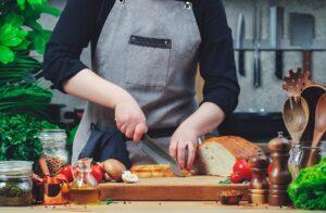 Blogger chef cutting white wheat bread on cozy kitchen with wooden table, kitchenware