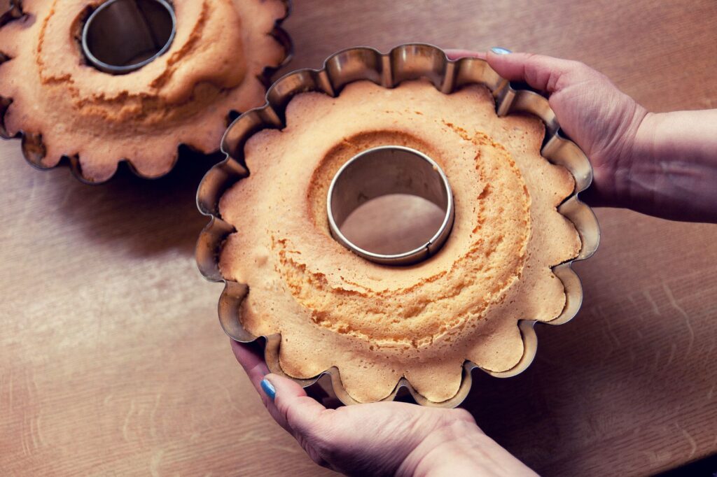 Un gâteau fraîchement cuit dans un moule cannelé tenu dans les mains au-dessus d'une table de cuisine.