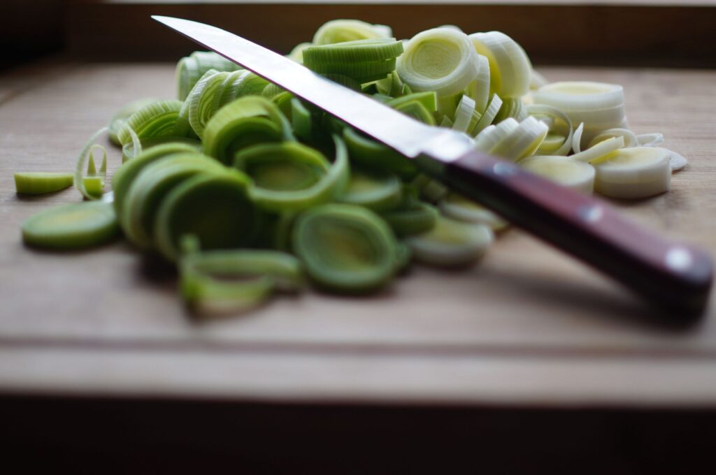 Poireaux fraîchement tranchés sur une planche à découper en bois avec un couteau aiguisé, idéal pour les thèmes de cuisine et de préparation alimentaire.