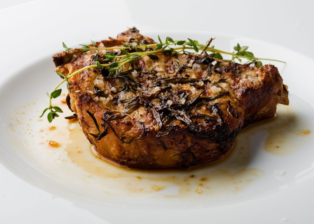 Délicieuse côtelette de porc en croûte d'herbes servie sur une assiette blanche, garnie de thym frais.