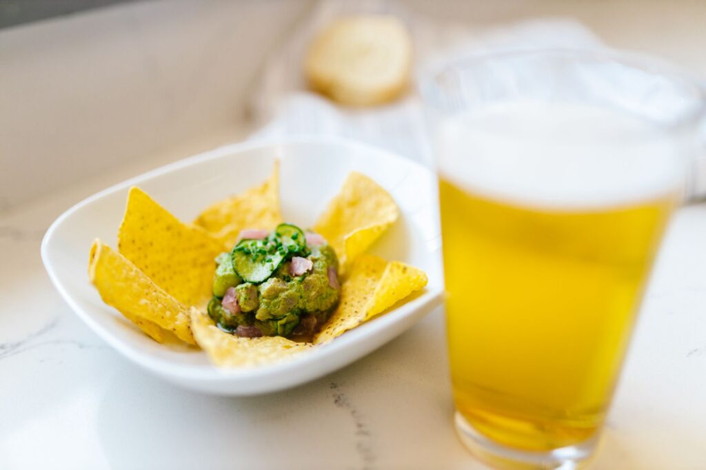 Un verre de bière frais avec un bol de guacamole et des chips de tortilla sur un comptoir de cuisine.