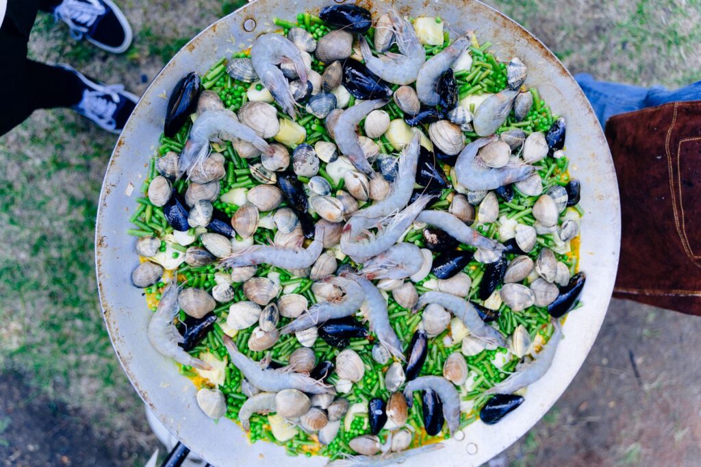 Gros plan sur une paella de fruits de mer crue avec des palourdes, des moules et des crevettes dans une grande poêle en plein air. Parfait pour le voyage culinaire.