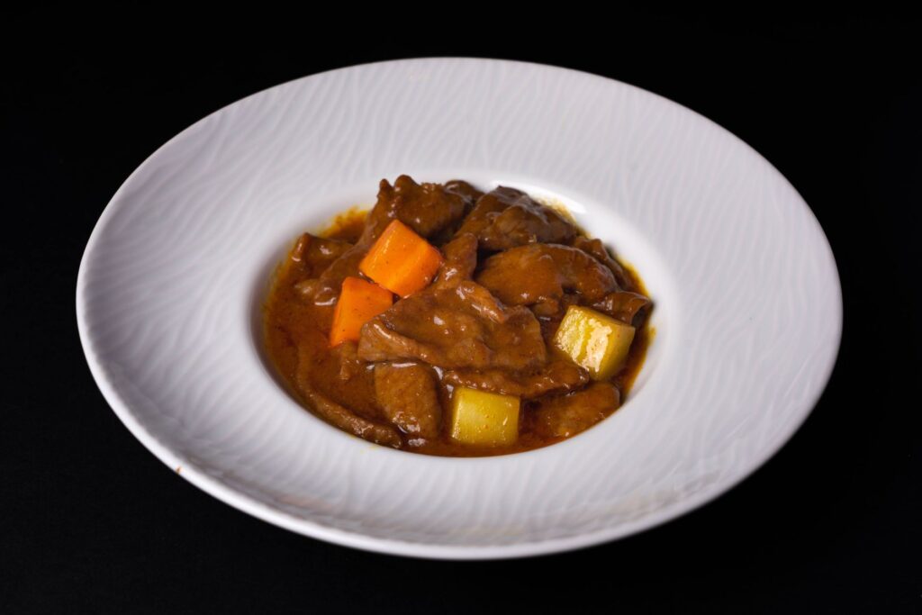 Délicieux ragoût de boeuf avec des carottes et des pommes de terre servi dans un bol en céramique blanc sur un fond sombre.