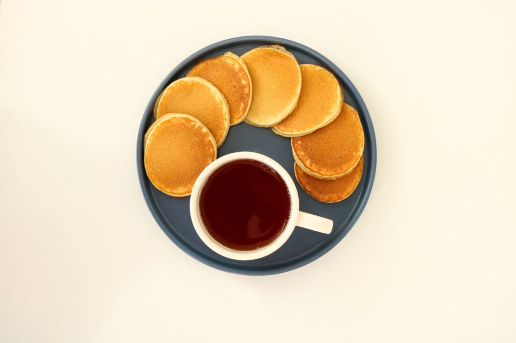 Une assiette de pancakes dorés avec une tasse de café chaud sur un fond blanc.
