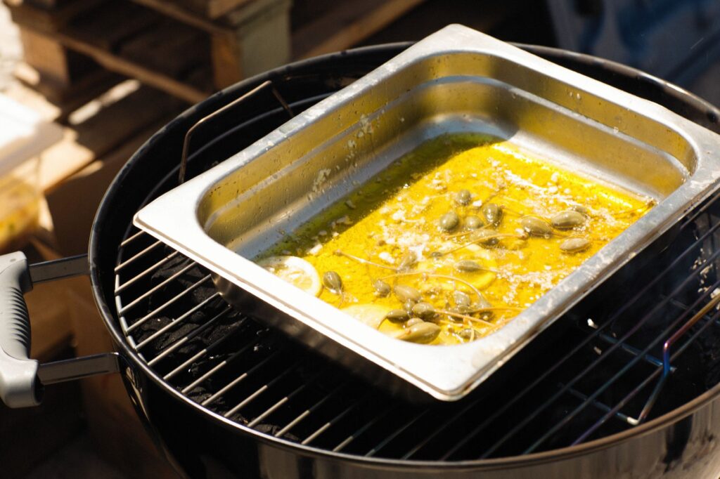 Cuisine en plein air avec des tranches de citron et de l'huile d'olive dans un plateau en acier inoxydable sur un barbecue.