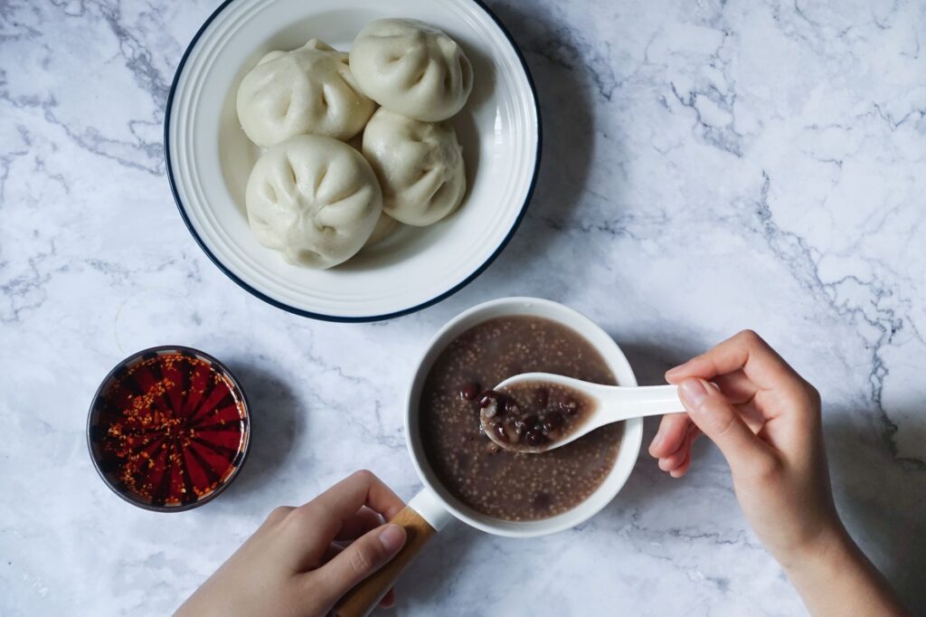Vue de dessus de baozi, soupe de haricots rouges et sauce chili sur une table en marbre.