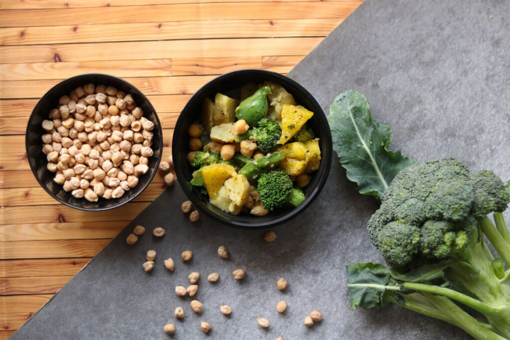 Vue de dessus de pois chiches, brocoli et salade de légumes mélangés dans des bols noirs sur une surface en bois.
