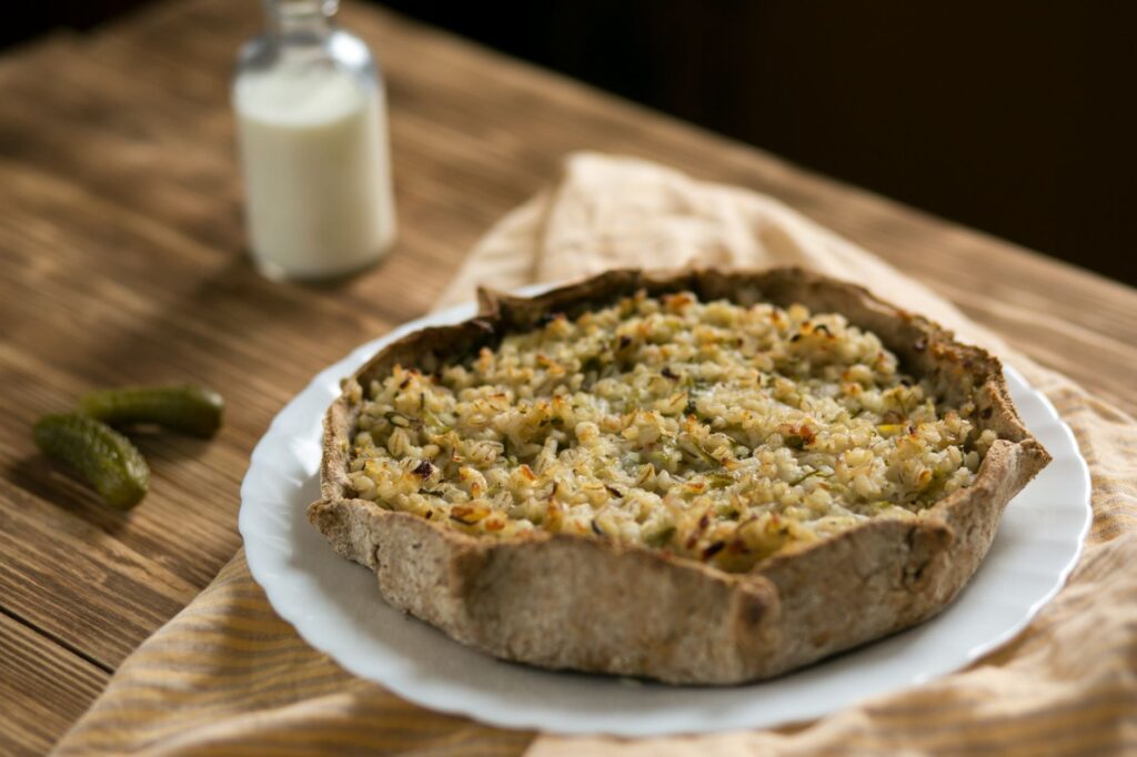 Quiche rustique maison avec des grains servie sur une assiette blanche avec du lait et des cornichons.