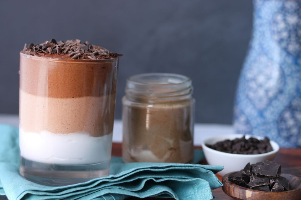 Délicieuse mousse au chocolat en couches dans un verre transparent avec des copeaux de chocolat, à côté des ingrédients.