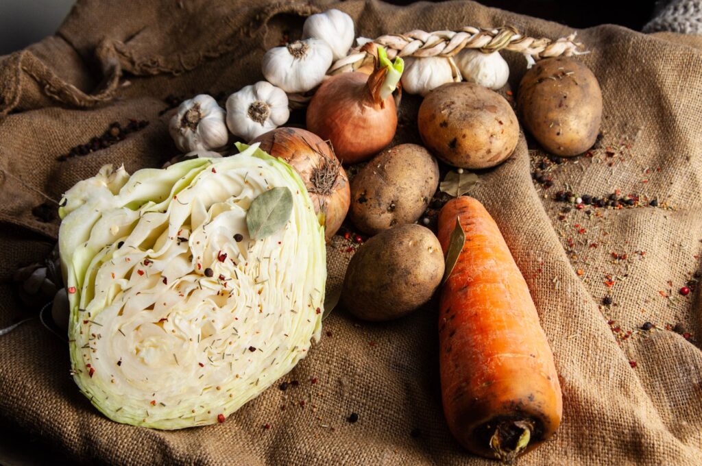 Une présentation naturelle de légumes biologiques comprenant du chou, de l'ail, des oignons, des pommes de terre et des carottes sur de la toile de jute.