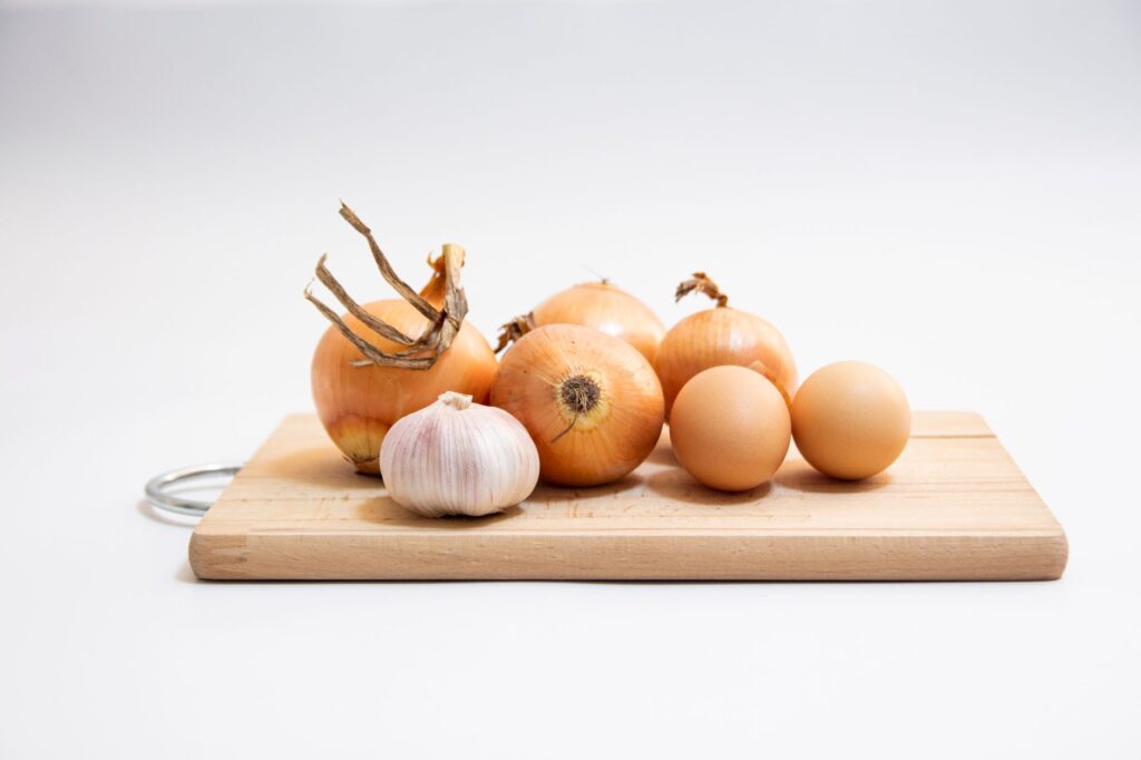 Des oignons biologiques et des gousses d'ail disposés sur une planche à découper en bois dans une cuisine minimaliste.