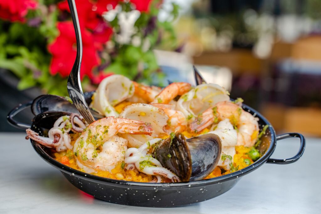 Gros plan d'un plat de paella aux fruits de mer dans une poêle noire, garni de crevettes, moules et calamars, servi en extérieur.