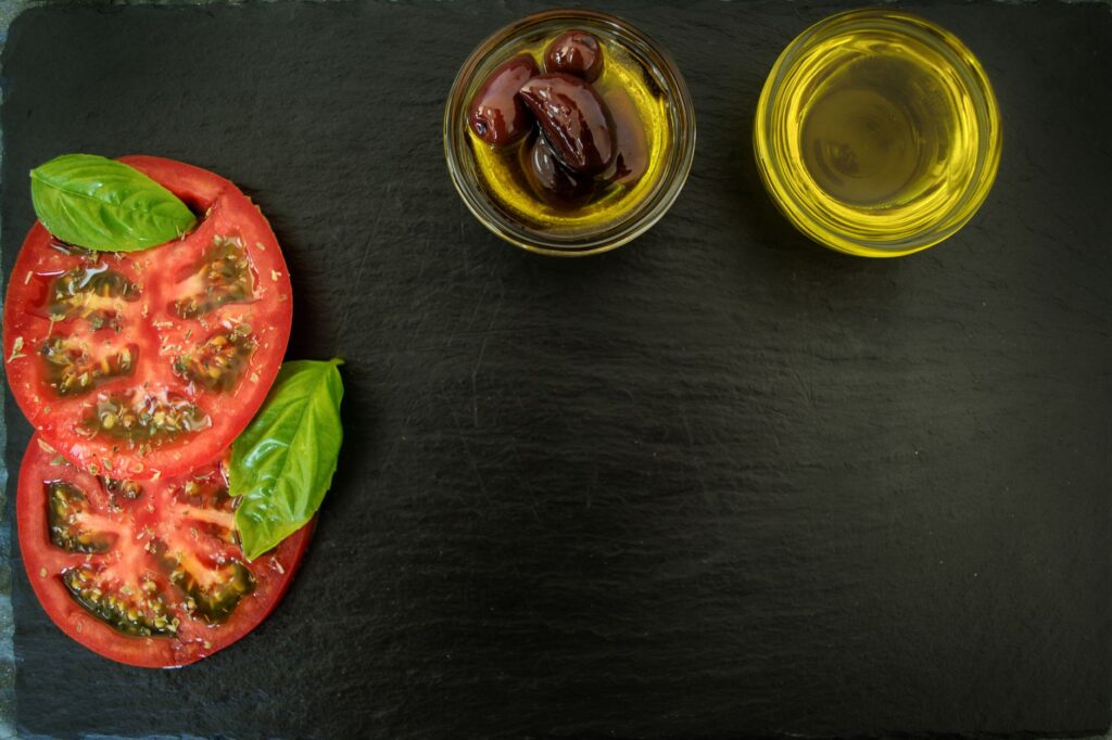 Vue de dessus de basilic frais, tomates tranchées, olives et huile d'olive sur ardoise, parfait pour des thèmes de cuisine italienne.