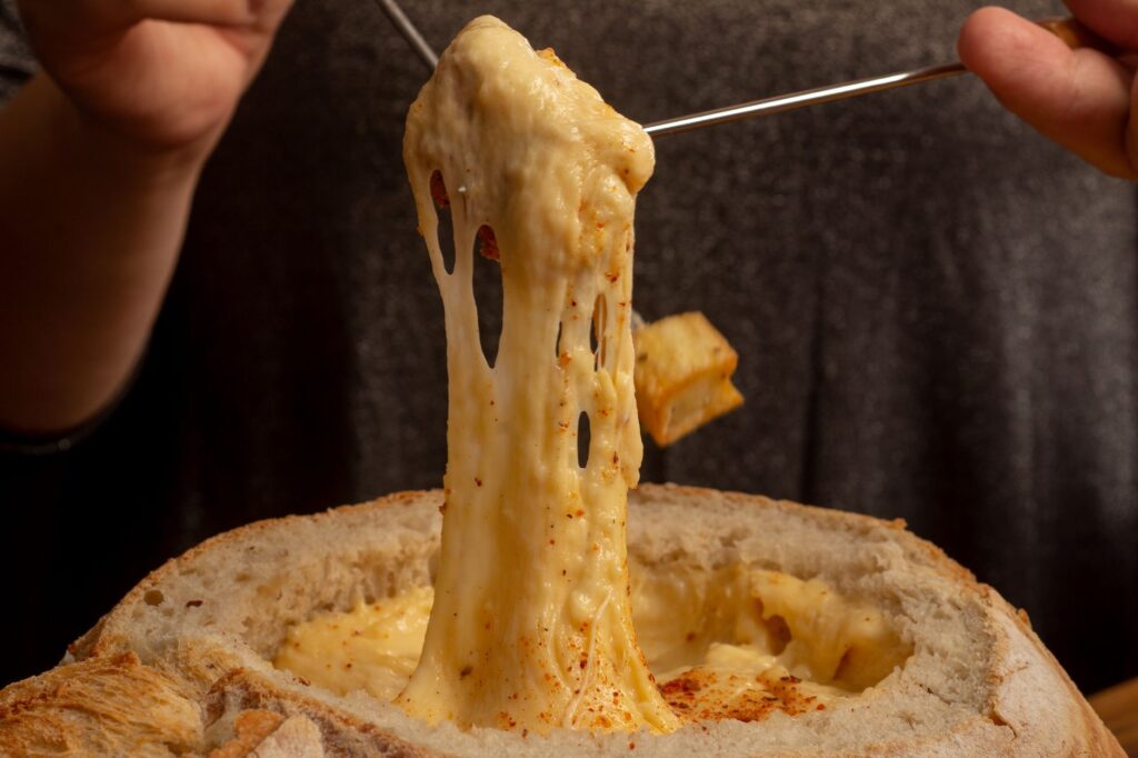 Gros plan alléchant de fondue au fromage fondu étirée d'un bol de pain.
