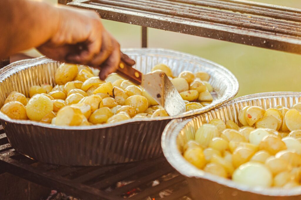 Gros plan sur des pommes de terre grillées dans des plateaux en aluminium à l'extérieur, mettant en avant un délicieux repas fait maison.