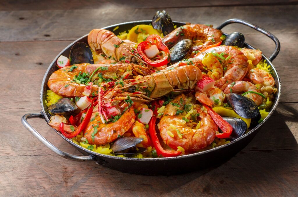 Paella de fruits de mer vibrante avec des crevettes, des moules et des légumes dans un cadre rustique en extérieur.