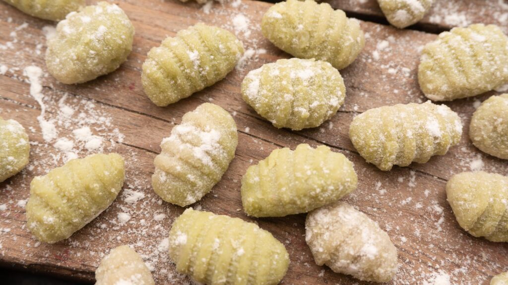 Des gnocchis verts parsemés sur une planche en bois rustique, saupoudrés de farine. Parfait pour les passionnés de cuisine.