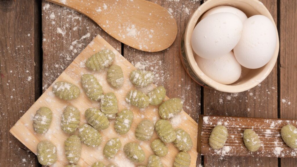Vue du dessus de gnocchis verts faits maison frais et des ingrédients pour cuisiner sur une table en bois rustique.