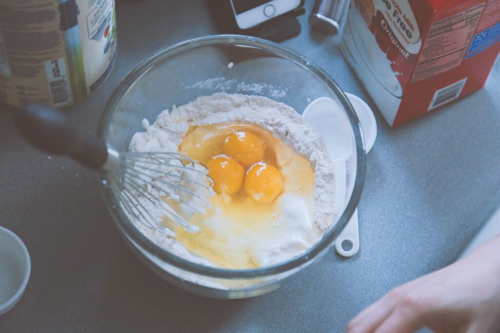 Gros plan sur le mélange de pâte à crêpes avec des œufs et de la farine dans un bol en verre.
