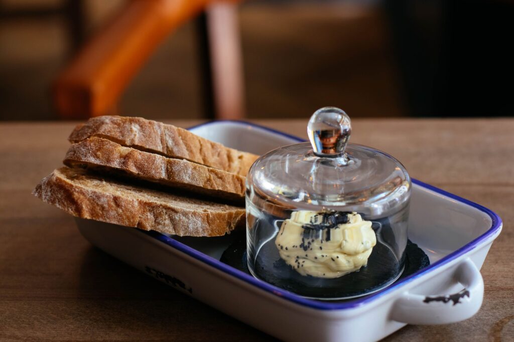 Tranches de pain de blé avec du beurre sous une cloche en verre, parfaites pour le petit-déjeuner ou le brunch.