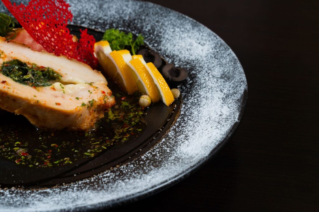 Gros plan sur un plat de poitrine de poulet gourmet garni de citron et d'herbes sur une assiette élégante.