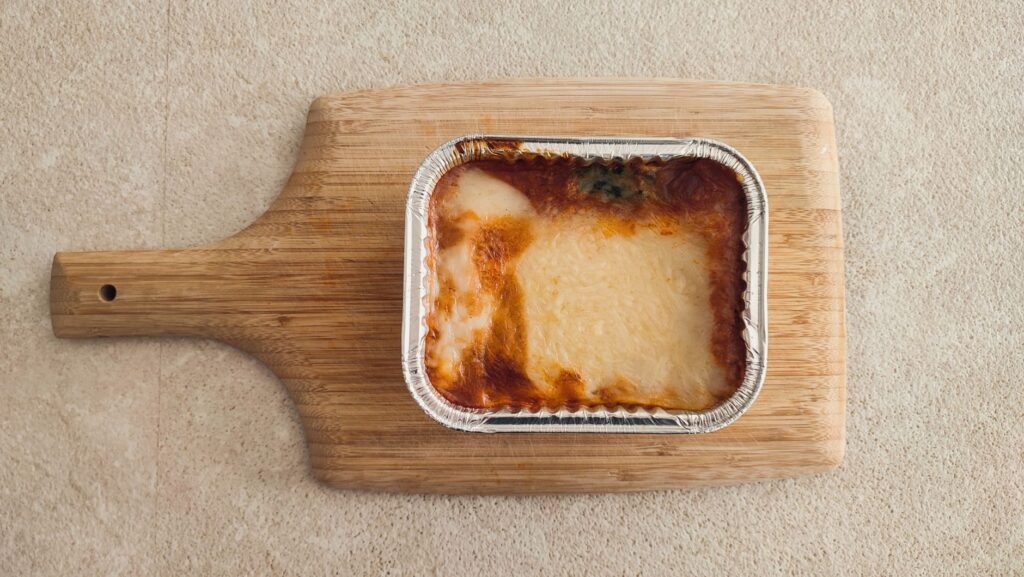 Délicieuse lasagne au fromage servie dans un plat en aluminium sur une planche en bois.