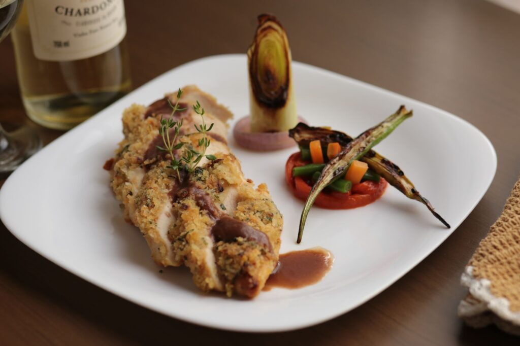 Plat de poulet gourmet avec des légumes grillés et un accord de vin, joliment dressé.
