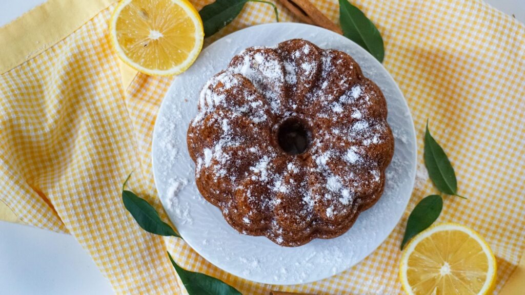 Délicieux gâteau bundt au citron garni de sucre glace, posé sur une assiette décorative avec des tranches de citron.