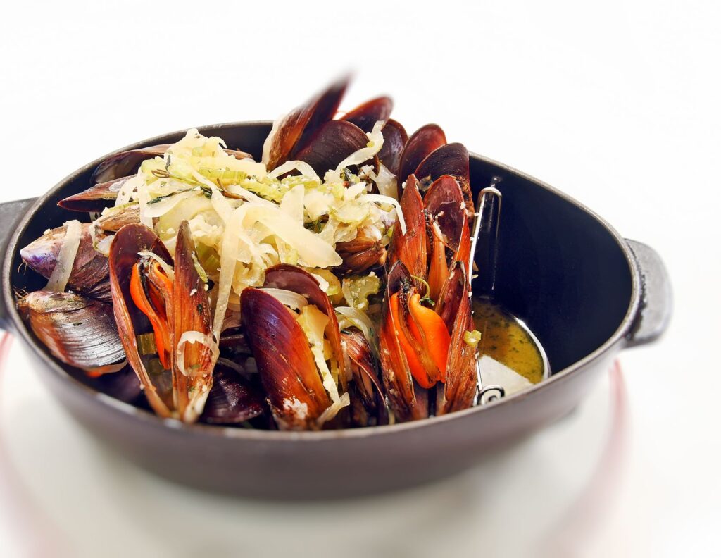 Délicieuses moules cuites à la vapeur garnies d'herbes dans une casserole noire sur fond blanc.