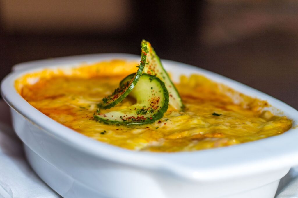 Gros plan d'une lasagne au fromage garnie de tranches de concombre, mettant en avant les riches saveurs italiennes.