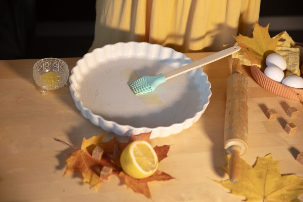 Plan rapproché d'un plat à tarte avec des ingrédients de pâtisserie sur une table en bois décorée de feuilles d'automne.