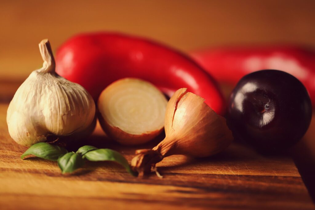 Un affichage vibrant d'ail frais, d'oignons, de poivrons, de basilic et de prunes sur une planche en bois.