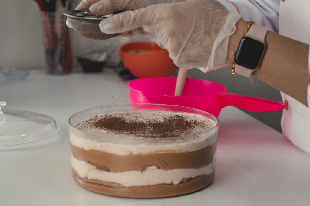 Gros plan d'un chef ajoutant méticuleusement de la poudre de cacao à un dessert étagé, mettant en valeur la précision culinaire.