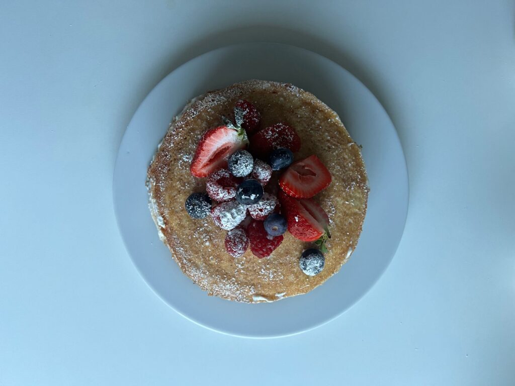 Pile de crêpes garnies de fraises fraîches, de myrtilles, de framboises et de sucre en poudre.