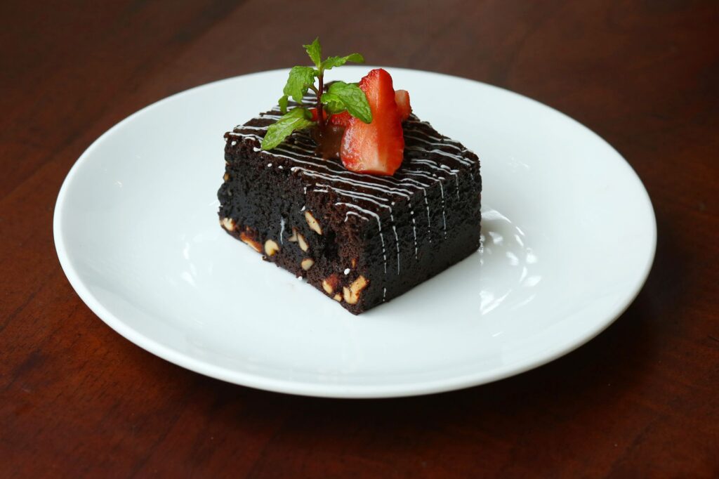 Brownie au chocolat riche garni de fraises et de menthe sur une assiette blanche.