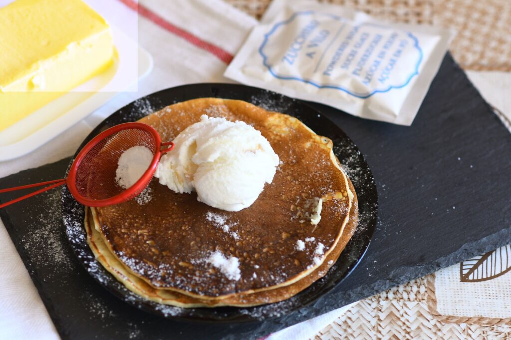 Gros plan de crêpes garnies de glace à la vanille et de sucre en poudre.