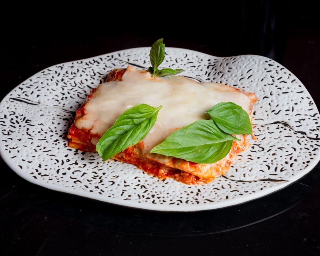 Lasagnes salées au fromage fondu et feuilles de basilic frais, présentées sur une assiette artistique.