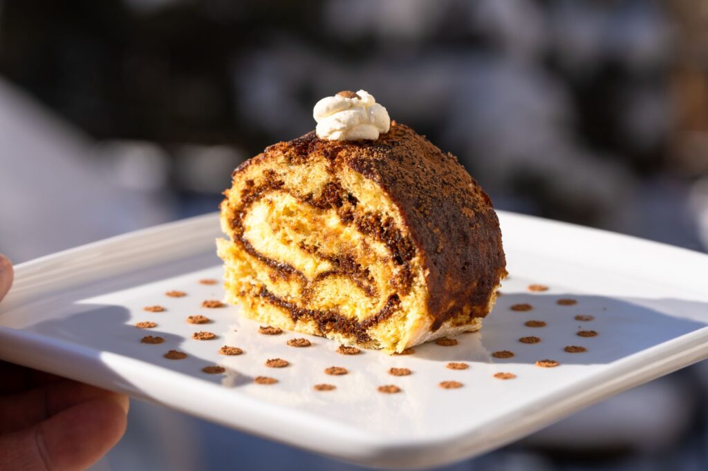Gros plan d'un rouleau de tiramisu fait maison garni de poudre de cacao sur une assiette blanche.