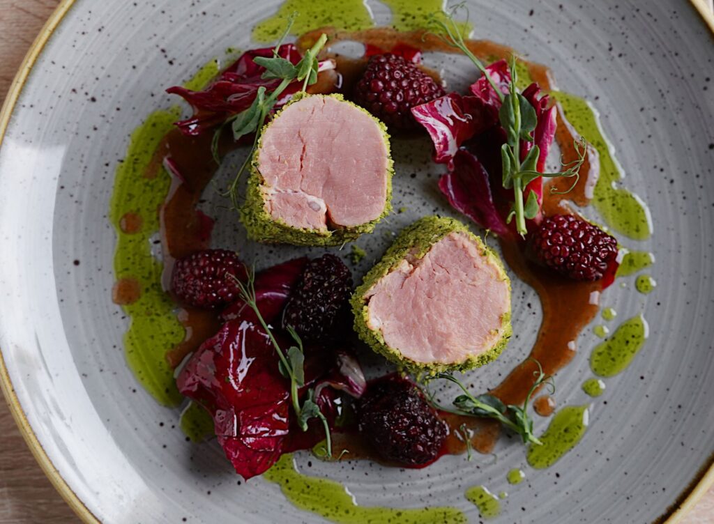 Plat élégant de filet de porc gourmet garni de framboises fraîches et de légumes verts vibrants.