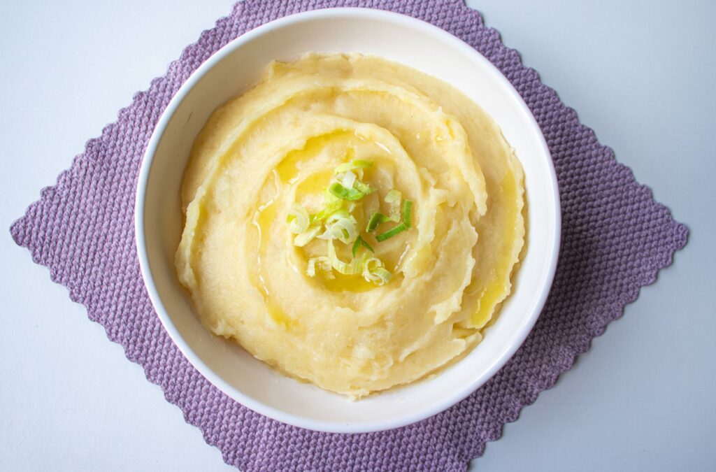Vue de dessus d'une purée de pommes de terre crémeuse garnie d'oignons verts dans un bol blanc.