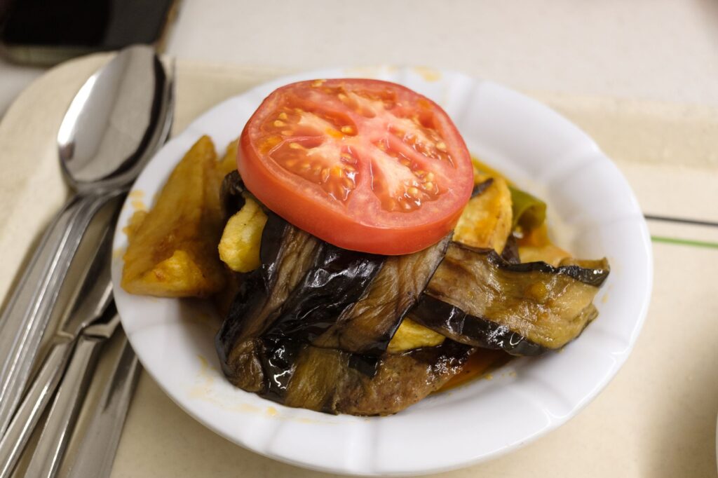 Une assiette de moussaka aux légumes mélangés avec une tranche de tomate et des aubergines grillées, servie dans un cadre de restaurant.