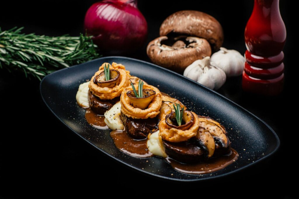 Filet de bœuf exquis garni de rondelles d'oignon, de champignons et de romarin sur une assiette noire.