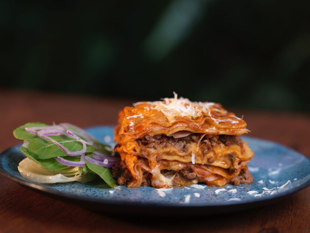 Gros plan sur une délicieuse lasagne maison servie avec une salade fraîche dans une assiette en céramique.
