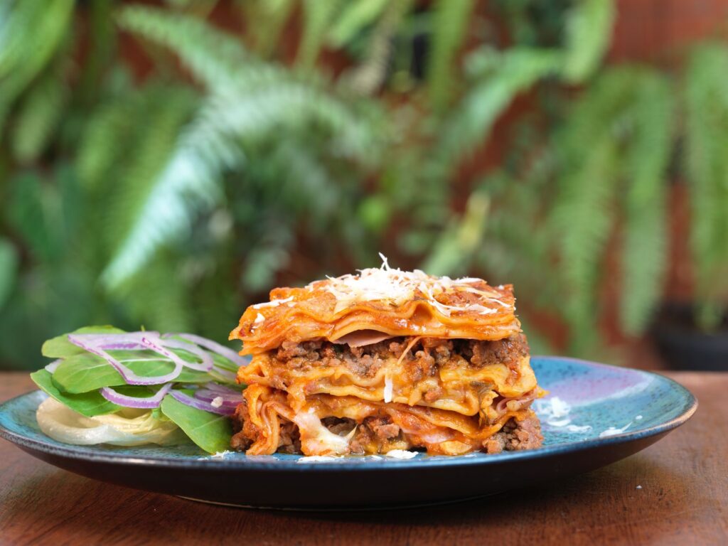Gros plan de lasagnes en couches avec salade d'accompagnement sur une assiette rustique.