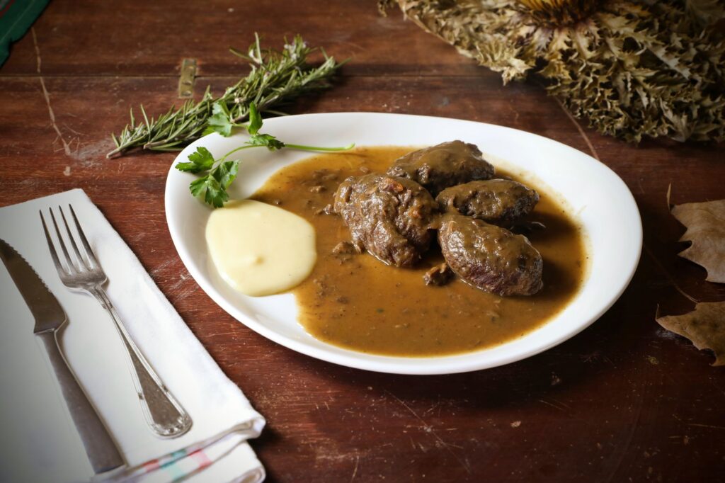 Délicieux bœuf en croûte d'herbes servi avec de la sauce et de la purée de pommes de terre crémeuse sur une table rustique.