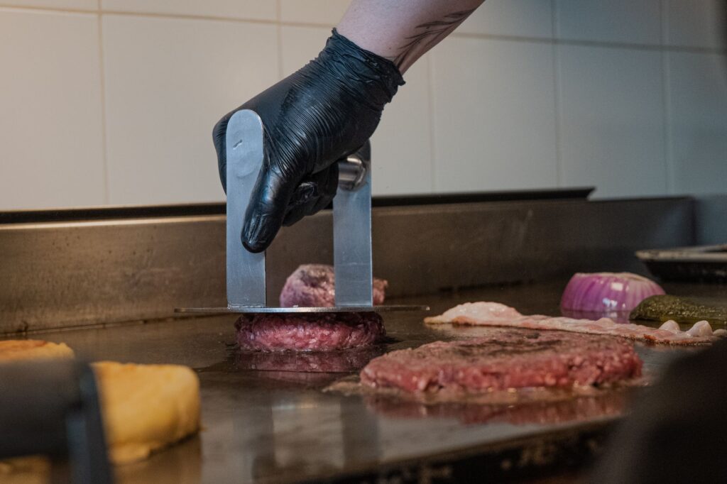Gros plan d'un chef cuisant un hamburger sur un gril à l'aide d'une presse en métal, à l'intérieur.