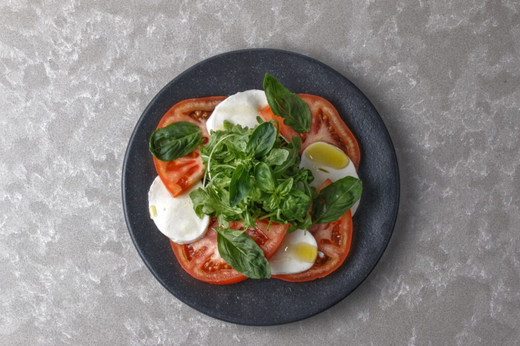 Vue de dessus d'une salade Caprese fraîche avec tomates, mozzarella et basilic sur une assiette sombre.